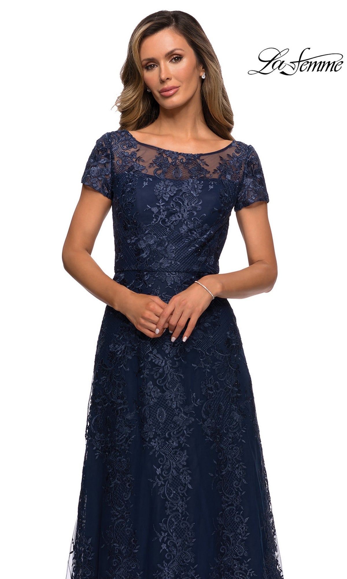 Woman in a navy blue Long Formal Dress: La Femme 27935 with floral lace, short sleeves, and sheer neckline stands against a white background. “La Femme” logo in top right corner.